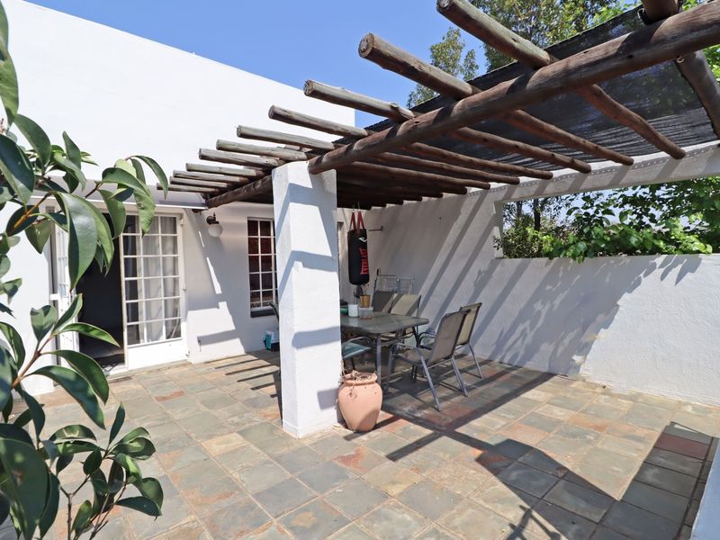 A covered outdoor patio area featuring a timber pergola, slate tile flooring, and direct access to the interior through white-framed french doors.