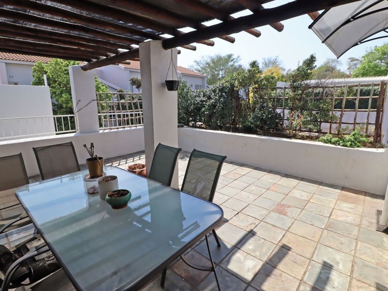 A covered outdoor patio featuring a timber pergola, tiled flooring, and a masonry boundary wall with integrated trellis screening.