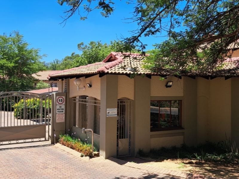 Front entrance view of the townhouse complex featuring a secure gated access point, guard house, and paved driveway.