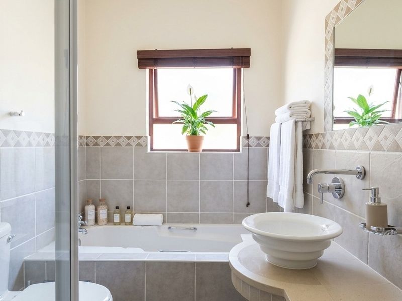 A well-maintained bathroom featuring a built-in bathtub, a modern vessel sink with wall-mounted tap, and neutral tiled finishes.