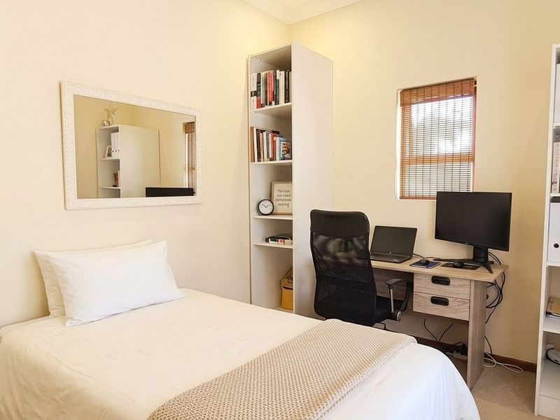 A functional bedroom featuring neutral walls, a window with blinds, and built-in electrical fixtures, suitable for use as a guest room or home office.