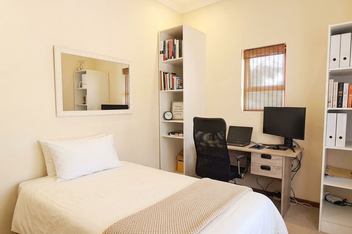 A functional bedroom featuring neutral walls, a window with blinds, and built-in electrical fixtures, suitable for use as a guest room or home office.