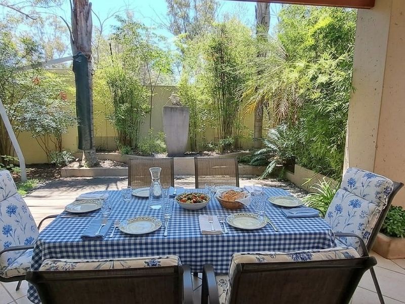 A covered outdoor patio area featuring tiled flooring and structural pillars, overlooking a landscaped garden with established greenery.