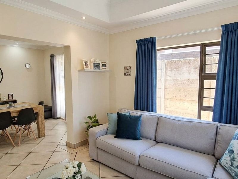 An open-plan living and dining area featuring tiled flooring, recessed ceiling details, and large windows allowing for natural light.