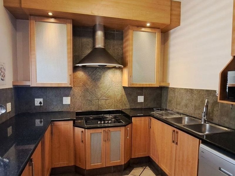 A functional kitchen featuring wood-finish cabinetry, granite countertops, a gas hob with extractor fan, and a double basin sink with tiled backsplash.