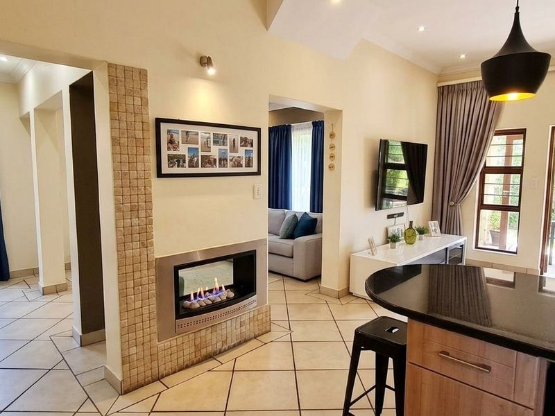 Spacious open-plan living area featuring a modern built-in fireplace, tiled flooring, and a kitchen island with granite countertops, flowing seamlessly to the outdoor patio.