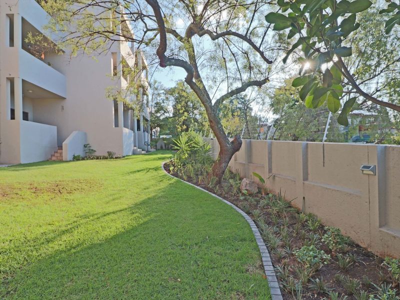 A well-maintained rear garden area featuring a manicured lawn, landscaped garden beds with paved edging, and a secure boundary wall with electric fencing.
