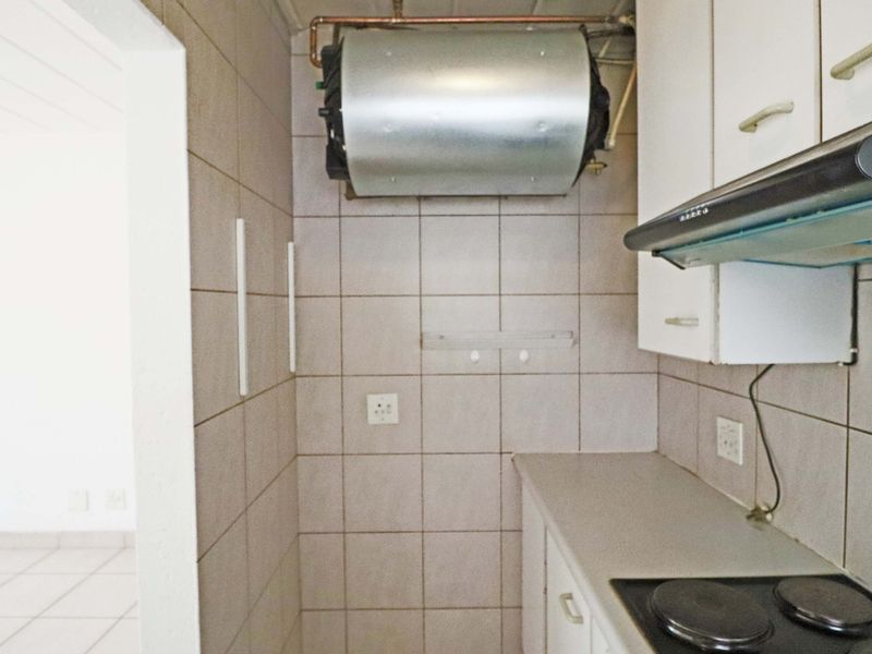 A compact kitchen area featuring tiled walls, built-in cabinetry, an electric hob with extractor fan, and an exposed wall-mounted water heater.