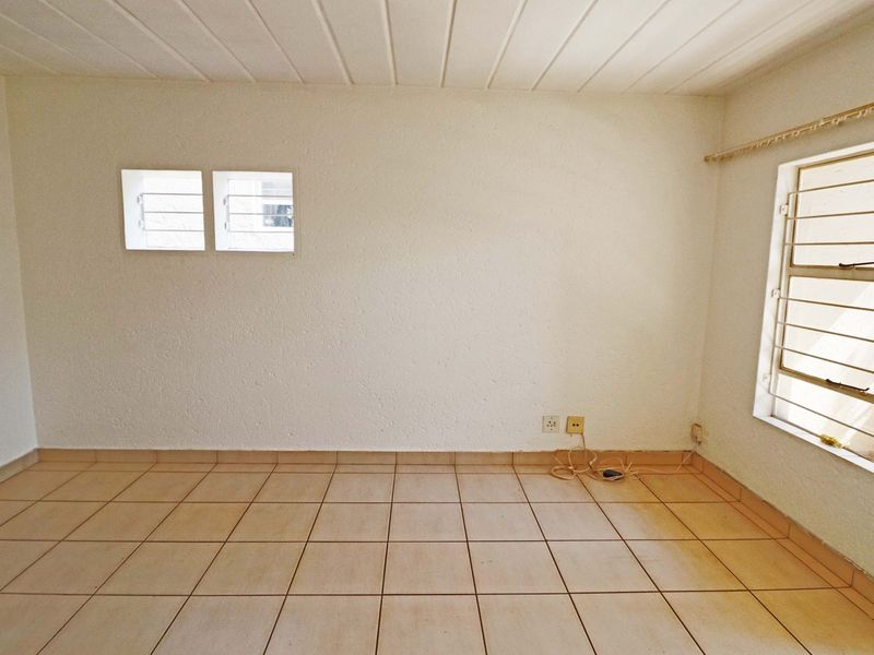 An empty bedroom featuring tiled flooring, louvered windows with security bars, and a tongue and groove ceiling.