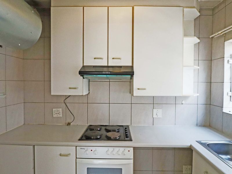 A functional kitchen featuring built-in cabinetry, an electric hob with extractor fan, and a stainless steel sink with tiled backsplash.