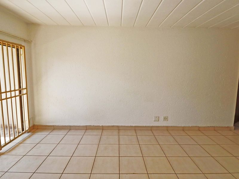 An empty living area featuring tiled flooring, a textured wall, and a security gate leading to an outdoor space.