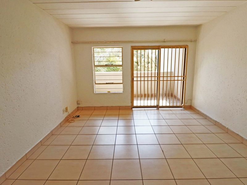An empty living room featuring tiled flooring, textured walls, and a sliding glass door with a security gate leading to an outdoor area.