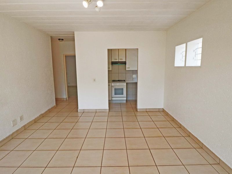 An open-plan living area featuring tiled flooring and a separate, compact kitchen equipped with built-in cabinetry and a freestanding stove.