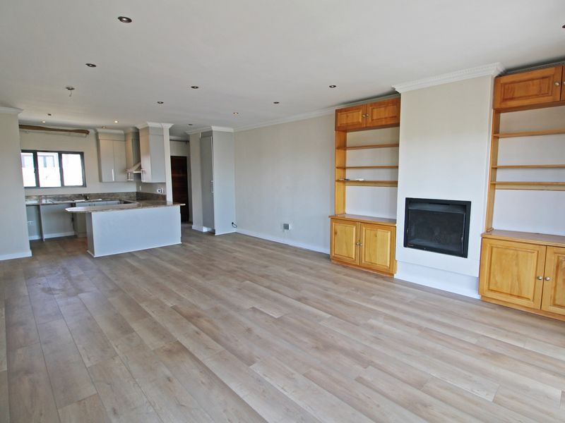 Spacious open-plan living area featuring modern laminate flooring, a built-in fireplace with surrounding cabinetry, and a functional kitchen with stone countertops.