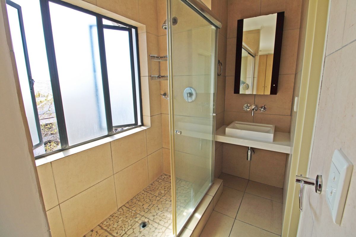 A clean, modern bathroom featuring a glass-enclosed shower, wall-mounted basin, and neutral floor-to-ceiling tiling.
