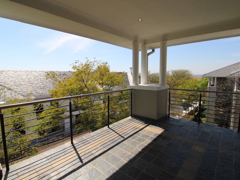 A spacious covered balcony featuring tiled flooring, a modern metal balustrade, and recessed ceiling lighting, offering an open outdoor area with neighborhood views.