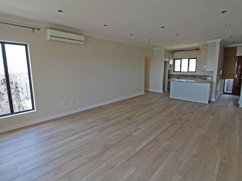 Spacious open-plan living area featuring modern laminate flooring, recessed lighting, an air conditioning unit, and a functional kitchen with an island.