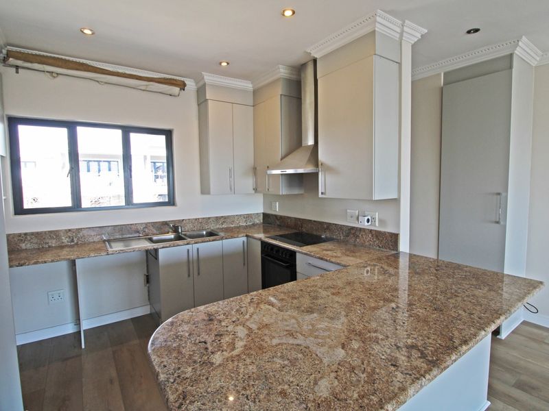 Modern kitchen featuring granite countertops, built-in oven, electric hob, stainless steel extractor fan, and ample cabinetry in a clean, open-plan layout.