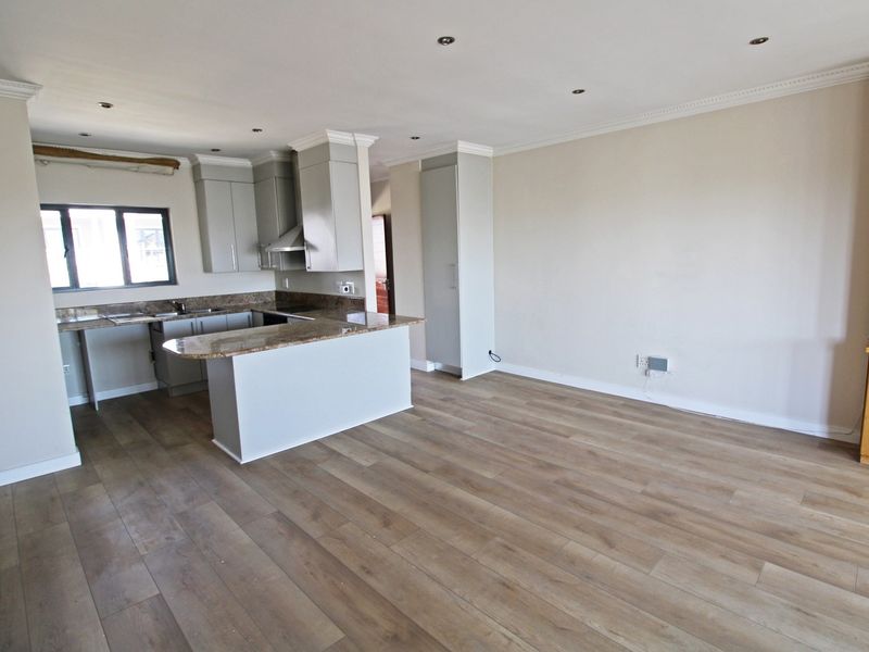 Spacious open-plan living area featuring modern laminate flooring, recessed lighting, and a functional kitchen with granite countertops and ample built-in cabinetry.