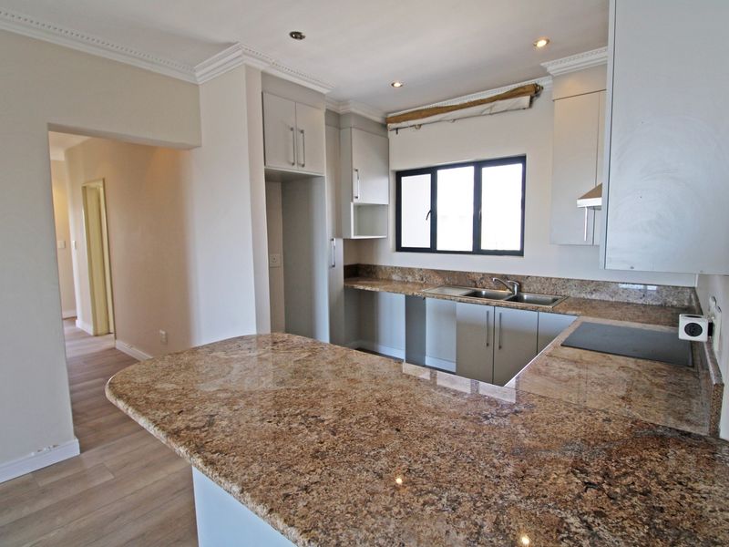 A clean, modern kitchen featuring granite countertops, ample built-in cabinetry, a double basin sink, and recessed lighting, offering a functional and bright workspace.