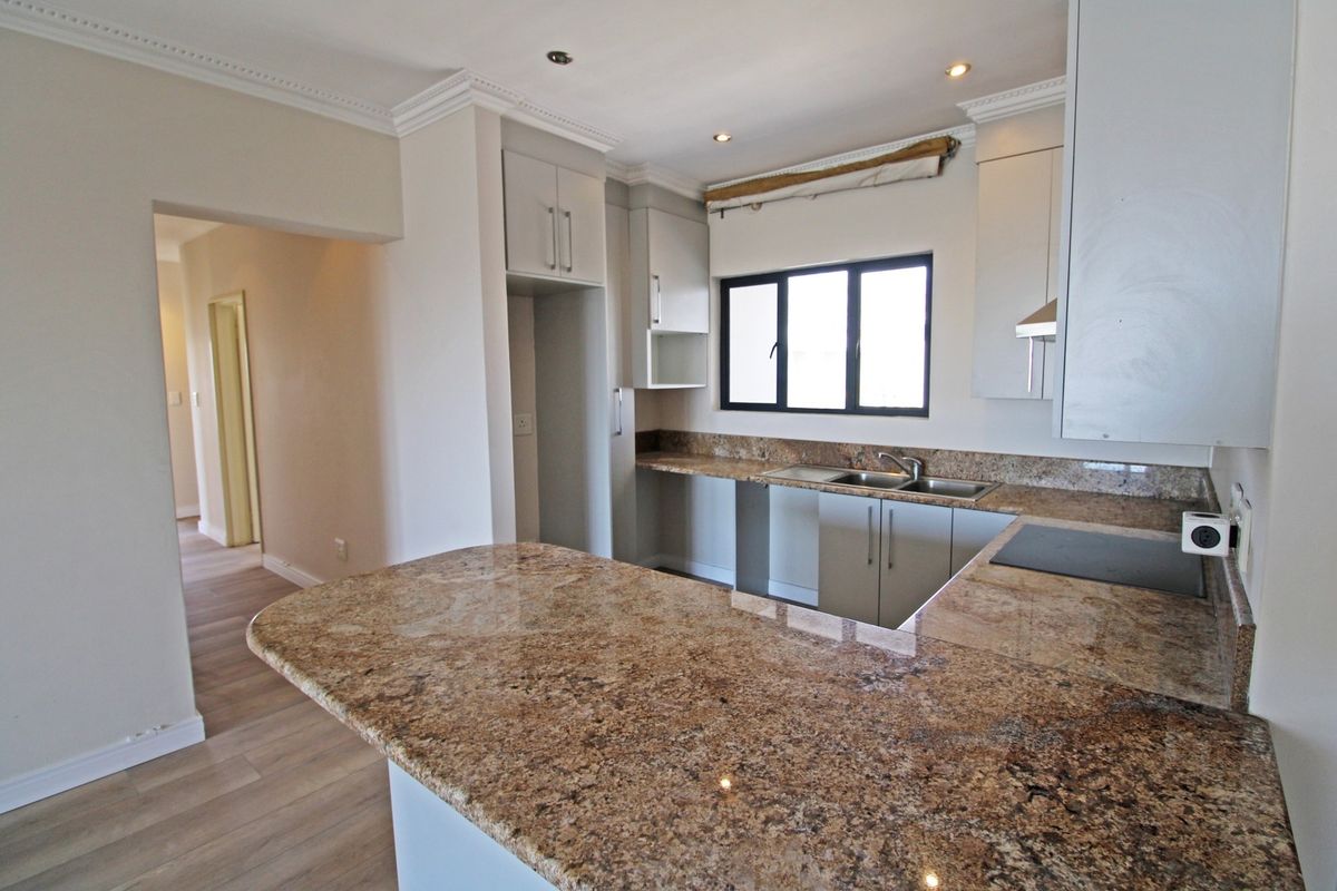 A clean, modern kitchen featuring granite countertops, ample built-in cabinetry, a double basin sink, and recessed lighting, offering a functional and bright workspace.