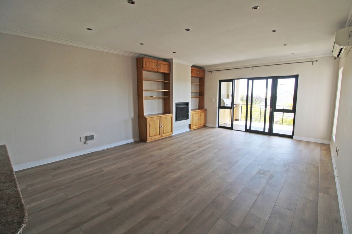Spacious living room featuring wood-look laminate flooring, built-in cabinetry with a fireplace, and sliding glass doors leading to an outdoor balcony.