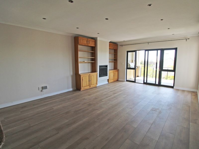 Spacious living room featuring wood-look laminate flooring, built-in cabinetry with a fireplace, and sliding glass doors leading to an outdoor balcony.