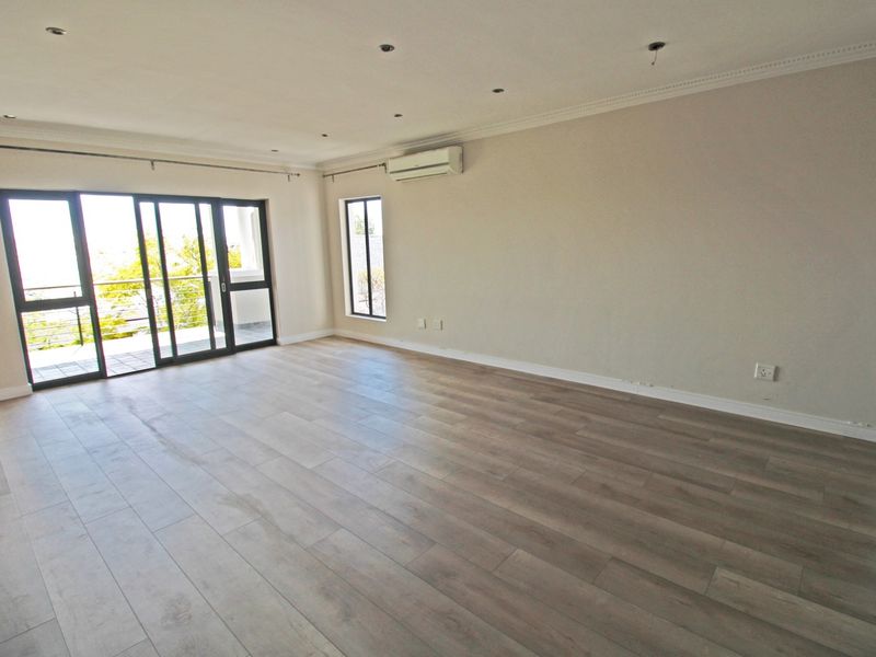 Spacious open-plan living area featuring light-toned laminate flooring, split-system air conditioning, and large sliding glass doors leading to an outdoor balcony.