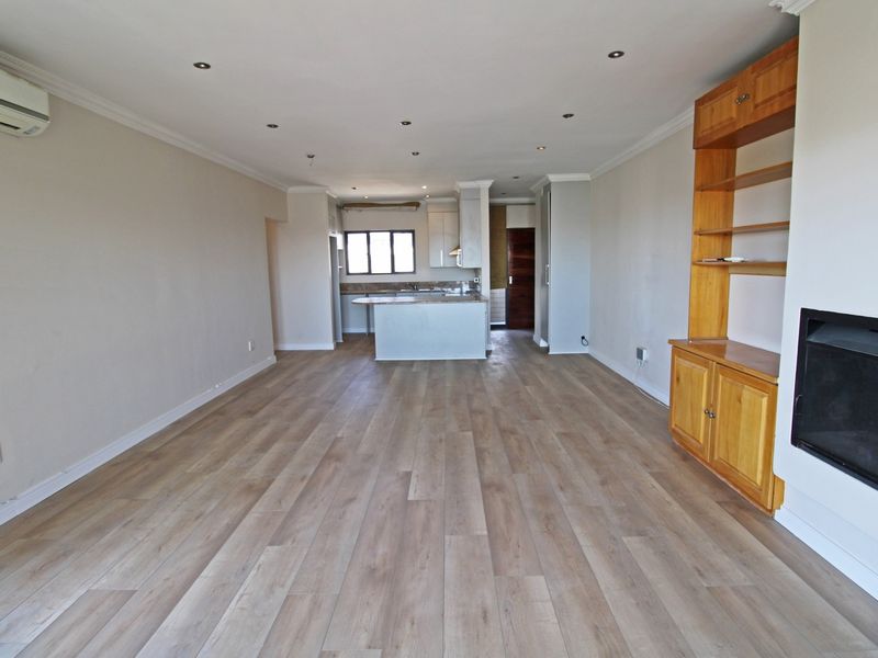Spacious open-plan living area featuring laminate flooring, recessed lighting, a built-in fireplace with shelving, and an integrated kitchen with island.