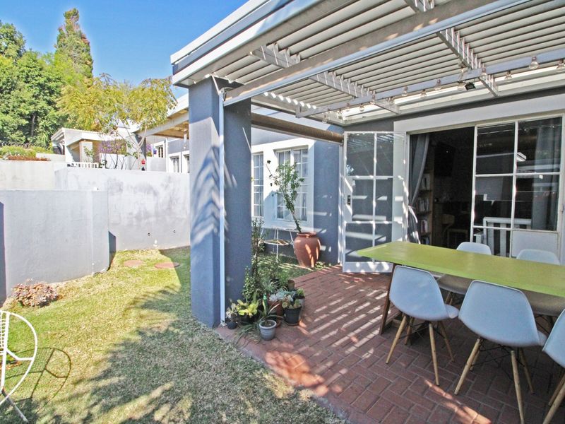 A covered outdoor patio area featuring brick paving and a louvred pergola, providing direct access to the interior through glass french doors.