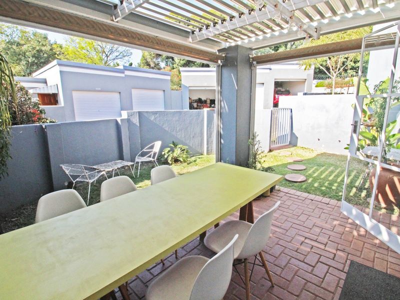 Covered patio area featuring brick paving and a pergola, providing a seamless transition to the private garden space.