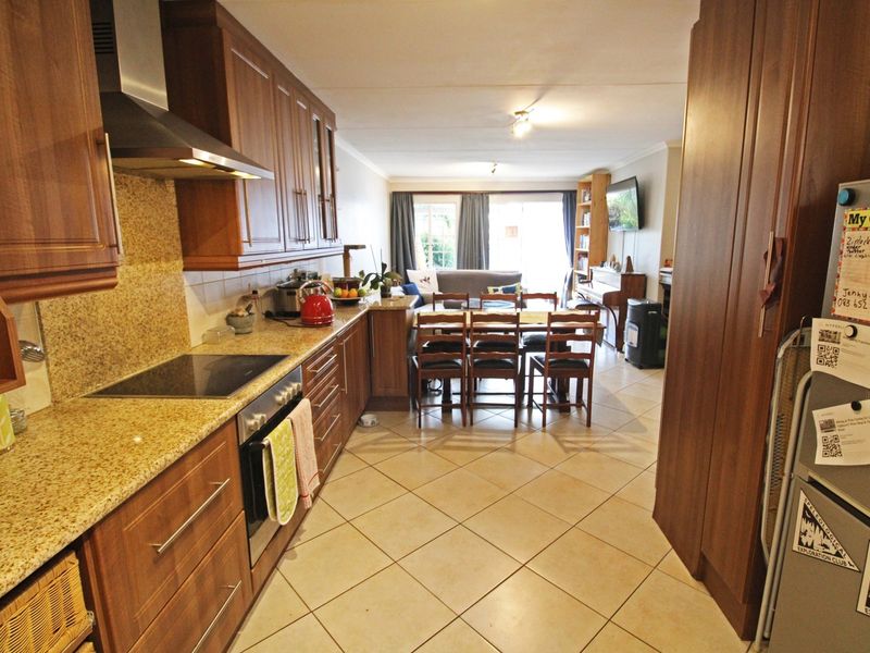 Open-plan kitchen and living area featuring wooden cabinetry, granite countertops, integrated appliances, and tiled flooring throughout the space.