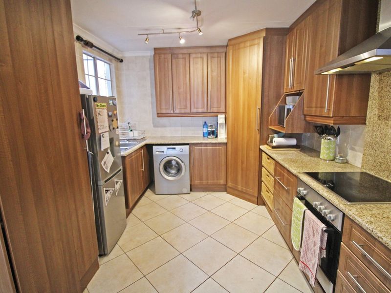 A functional kitchen featuring warm-toned wooden cabinetry, granite countertops, integrated appliances, and tiled flooring, offering a practical layout for daily cooking and utility needs.