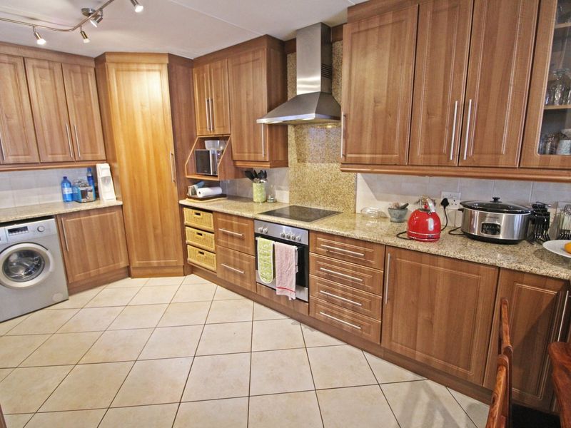 A functional kitchen featuring wood-finish cabinetry, granite countertops, a built-in oven with extractor fan, and integrated laundry facilities with tiled flooring.