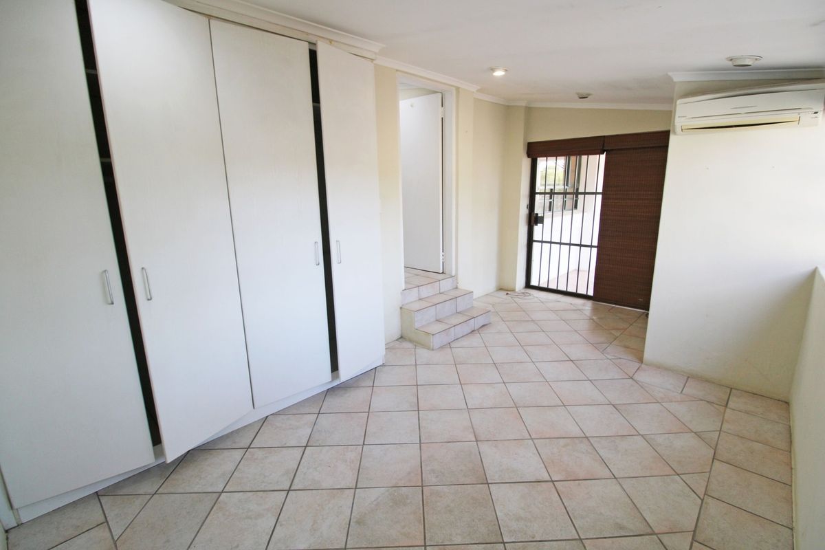 An empty bedroom featuring built-in cupboards, tiled flooring, a split-system air conditioner, and a security gate leading to an outdoor area.