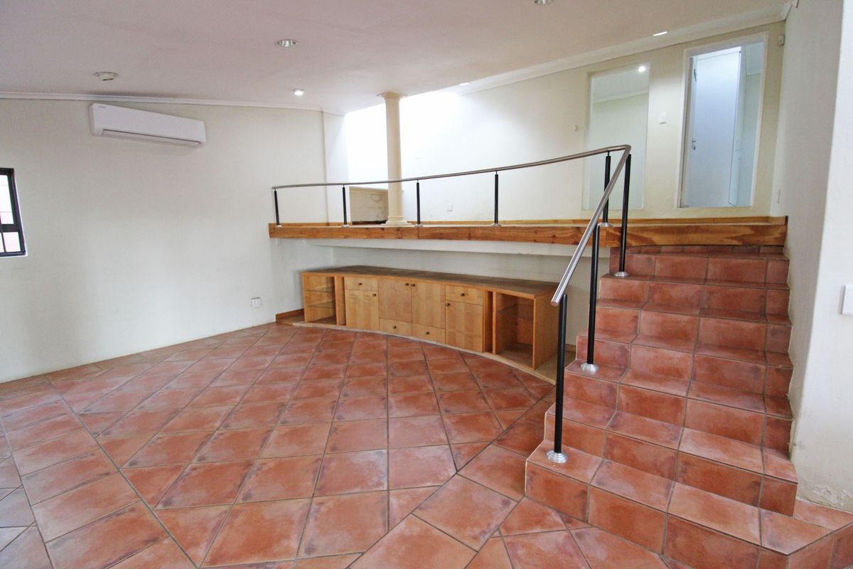Spacious living area featuring terracotta tiling, a raised platform with built-in cabinetry, and a modern metal balustrade, offering a versatile multi-level layout.