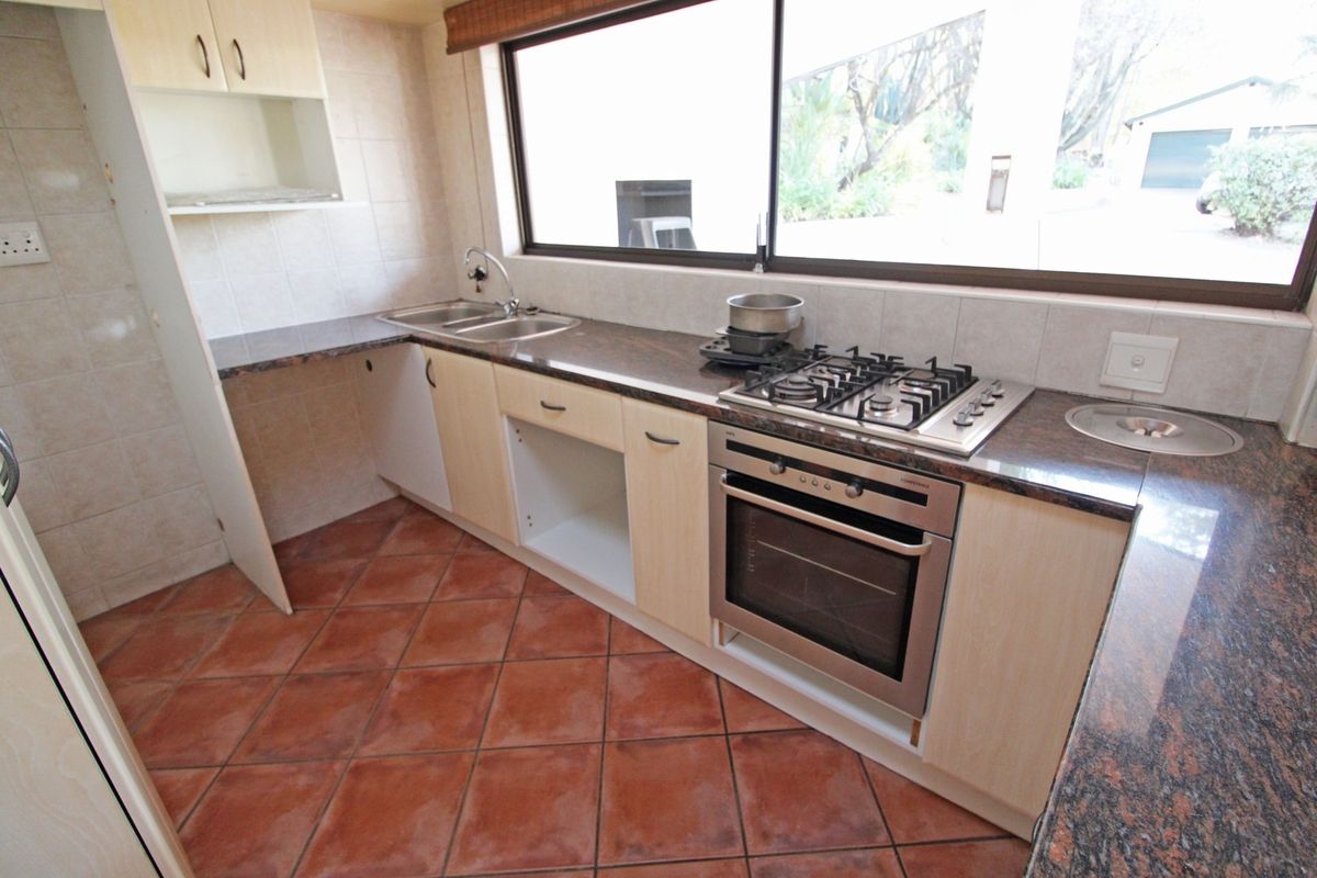 A functional kitchen featuring granite countertops, a gas hob, built-in oven, and tiled flooring, currently requiring minor cabinetry repairs.