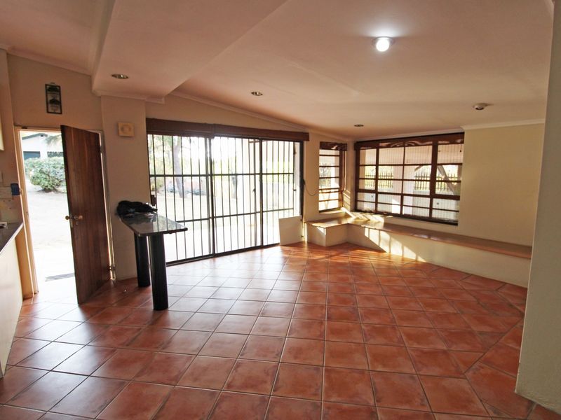 Spacious open-plan living area featuring terracotta floor tiles, a built-in window bench, and direct access to the exterior through security-gated sliding doors.