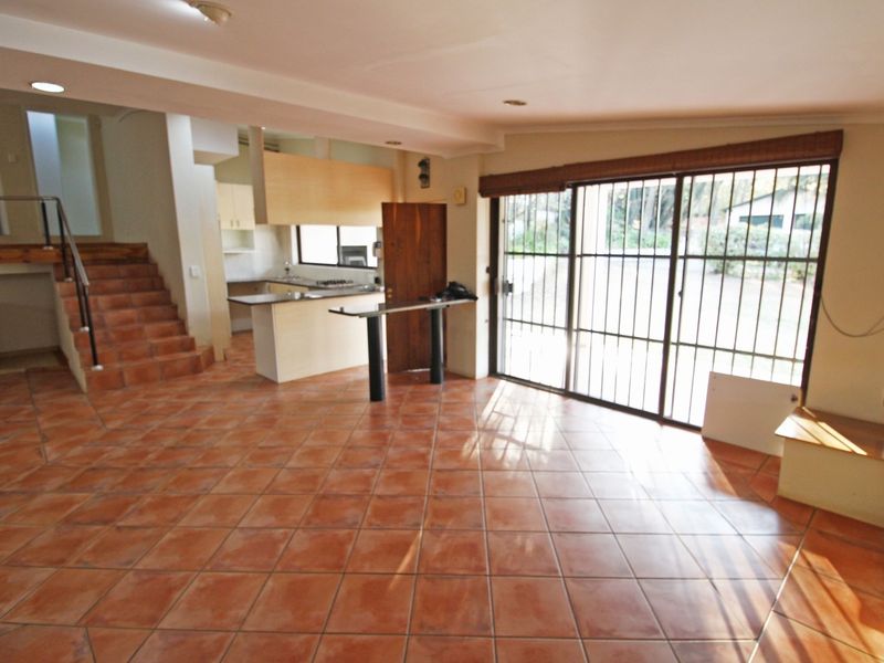 Spacious open-plan living area featuring terracotta-style tiled flooring, a functional kitchen with breakfast bar, and direct access to the exterior via sliding glass doors.