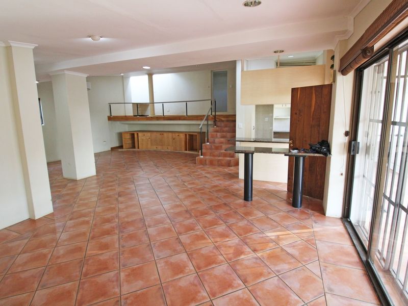Spacious open-plan living area featuring terracotta floor tiles, a raised platform with built-in cabinetry, and sliding glass doors leading to the exterior.