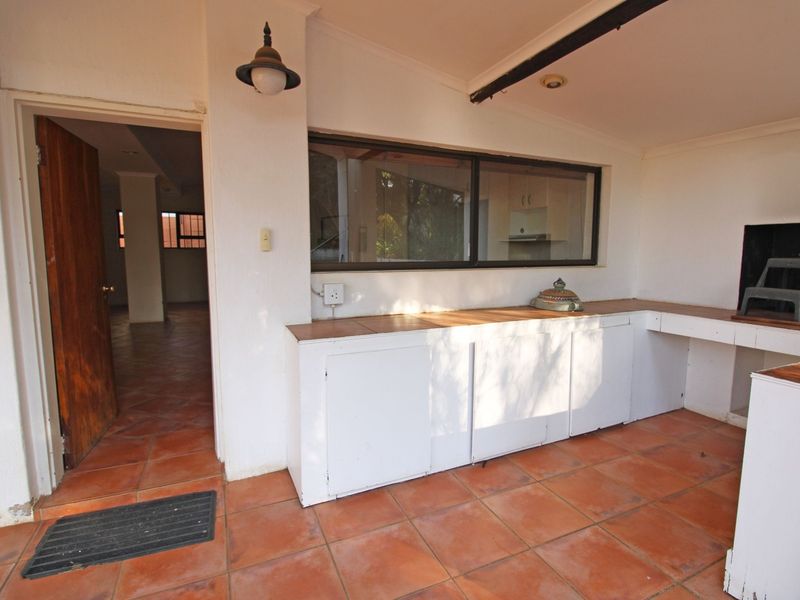 Covered patio area featuring built-in cabinetry, a built-in braai, and terracotta-style tiled flooring, providing a functional outdoor entertainment space.