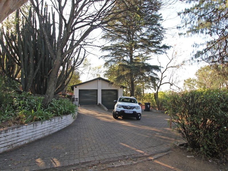A view of the property's front exterior featuring a paved driveway leading to a double garage with roller doors and established garden landscaping.