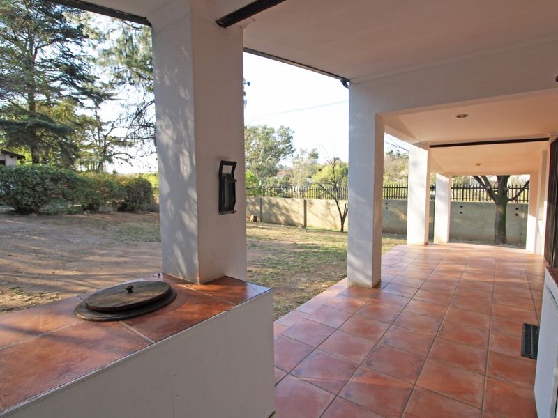 A covered patio area featuring tiled flooring, support pillars, and a built-in braai, overlooking the garden space.
