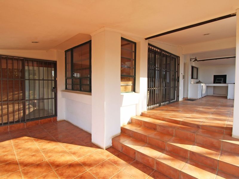 A spacious covered patio featuring tiled flooring, security gates, and a built-in braai area, perfect for outdoor entertaining.