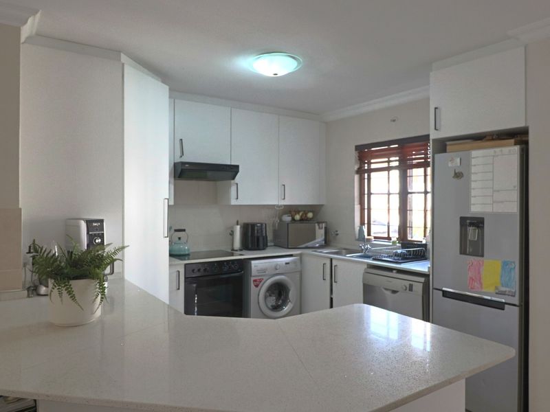Functional kitchen featuring white cabinetry, quartz countertops, built-in oven, hob, extractor fan, and integrated laundry plumbing, offering a clean and practical workspace.