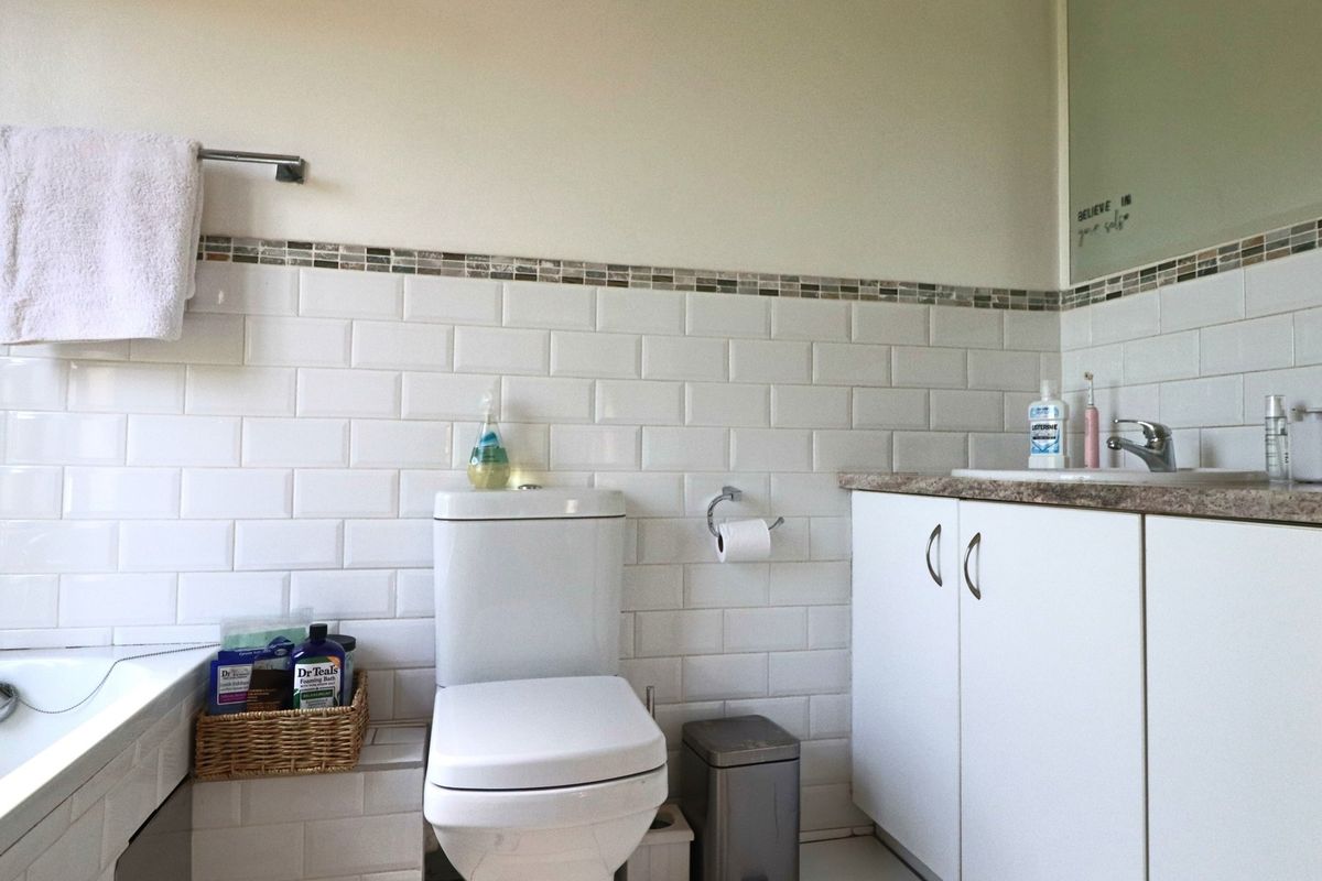 A clean bathroom featuring white subway wall tiles, a vanity cabinet with a laminate countertop, and a built-in bathtub.
