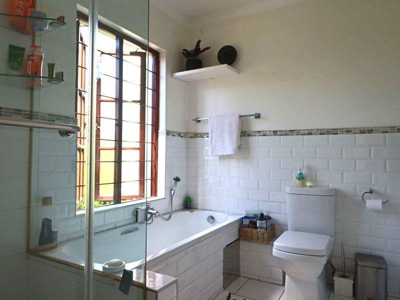 A functional bathroom featuring a built-in bathtub, subway tile wall finishes, a glass shower screen, and a window with security bars.