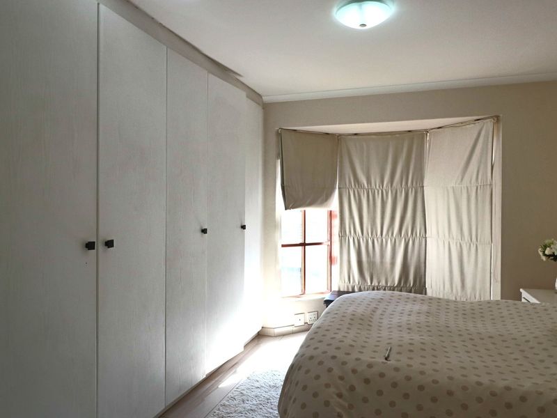 A well-lit bedroom featuring extensive built-in cupboards and a charming bay window with integrated blinds.