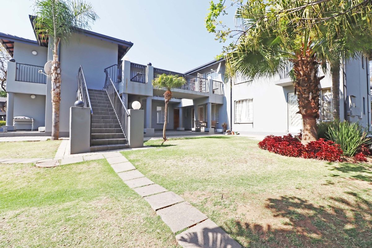 Rear view of the apartment complex featuring a communal garden, paved walkway, and an external staircase leading to the upper level balcony.