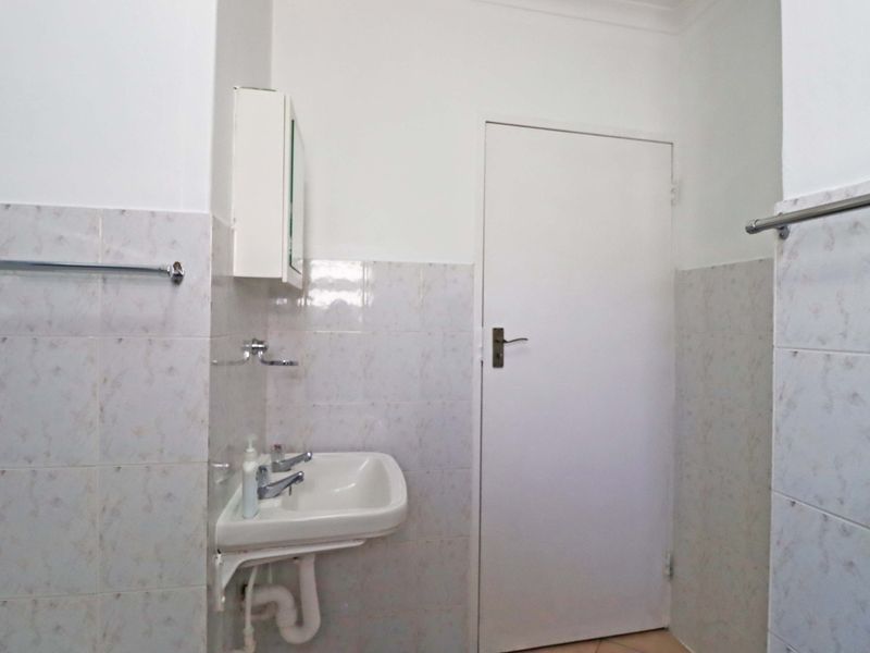 A functional bathroom featuring a wall-mounted basin, chrome fixtures, and tiled walls, providing a clean and practical space.